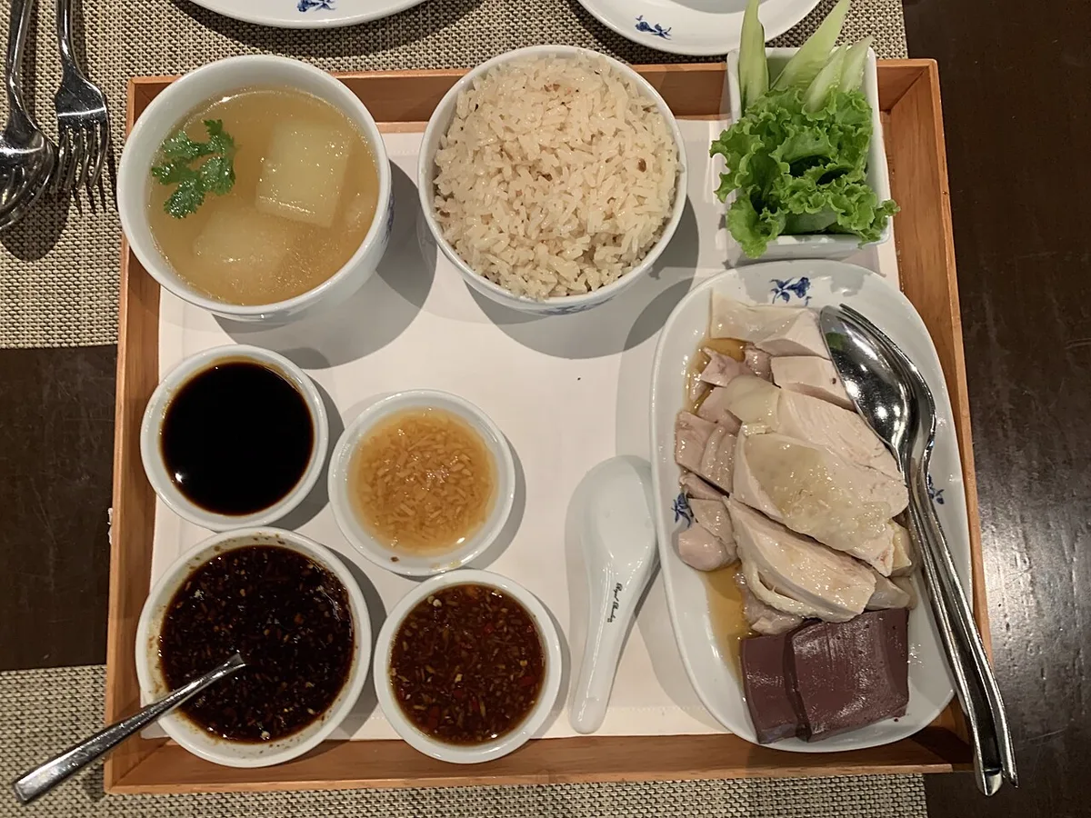 ข้าวมันไก่ไหหลำแบบชุดในกรุงเทพฯ มีไก่ต้มหั่นชิ้น เลือดไก่ ข้าวมัน ซุปฟัก และน้ำจิ้มสี่ถ้วย อาหารสายไหหลำที่เชื่อมกับแซ่ฝู แซ่ผู่
