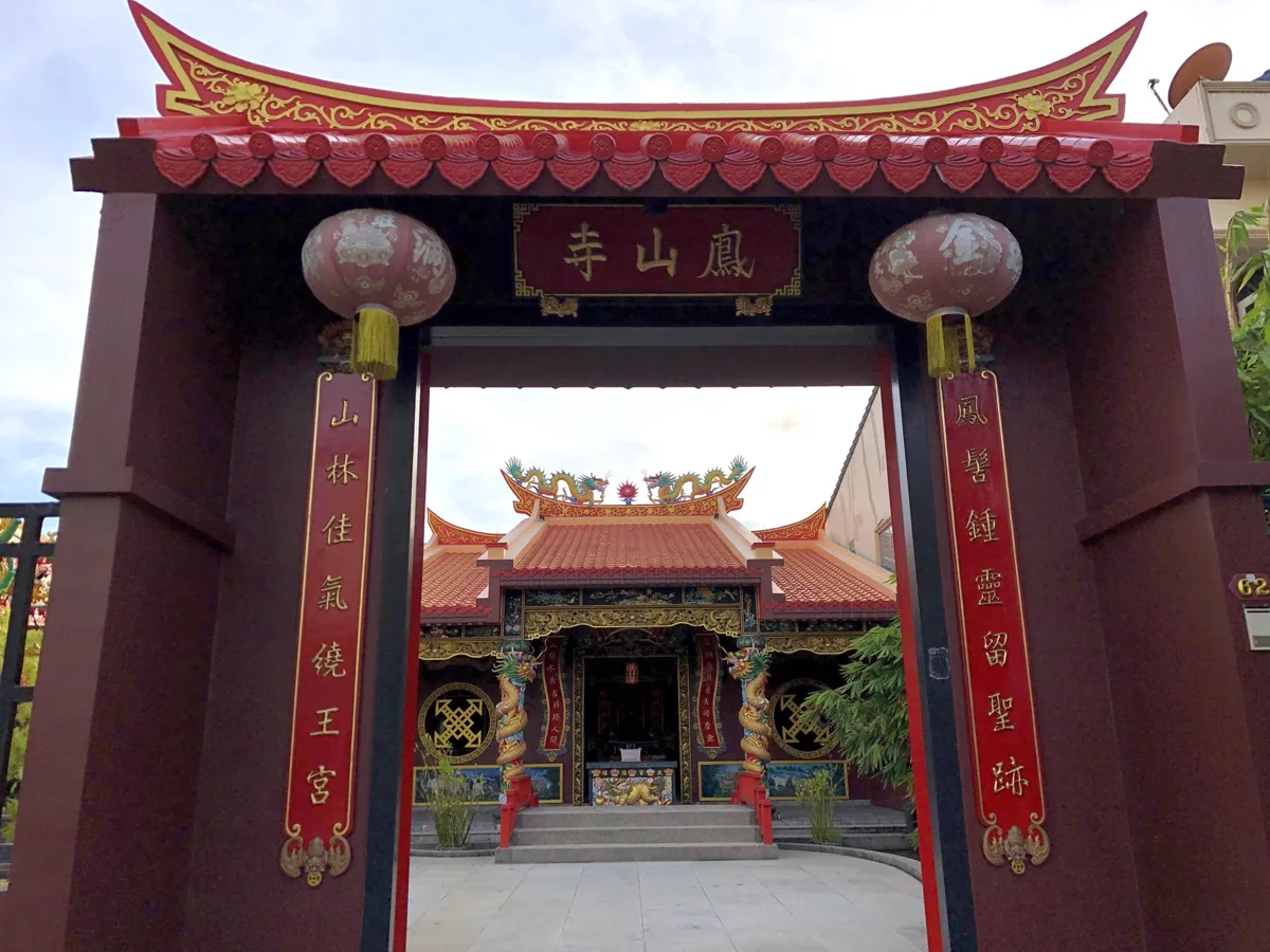 ประตูศาลเจ้าเฟิ่งซานซื่อ จังหวัดภูเก็ต ป้ายอักษรทอง 鳳山寺 และคู่คำขวัญสีแดงสองข้าง มองเห็นศาลเจ้าก๊วยเส้งอ๋อง เทพแซ่ก๊วย อยู่ด้านใน