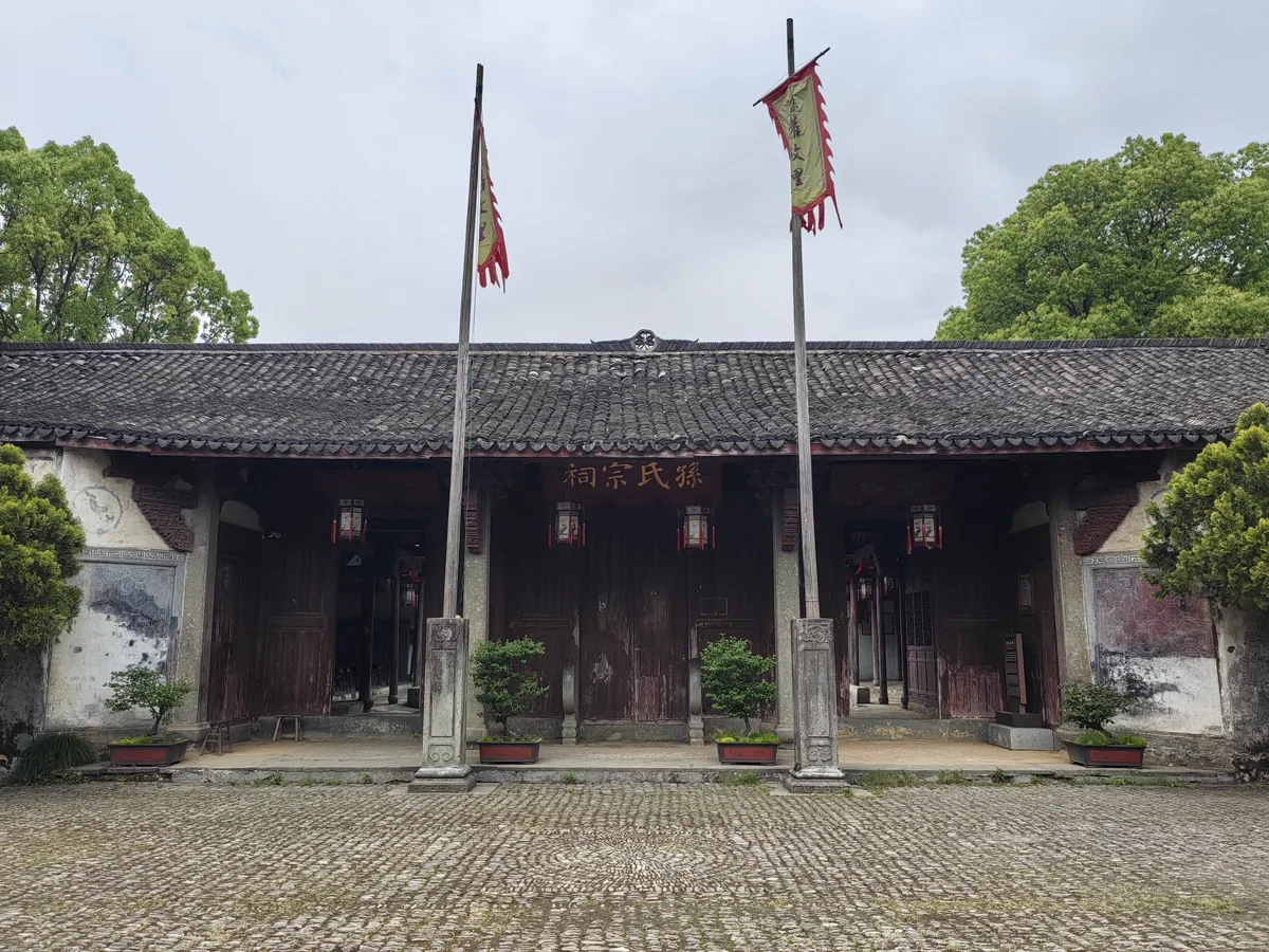 ด้านหน้าศาลบรรพชนแซ่ซึง แซ่ซุน 孫氏宗祠 ที่หลงเหมิน หลังคากระเบื้องดำ ป้ายชื่อเหนือประตูกลาง เสาธงสองต้น และลานหินกรวด