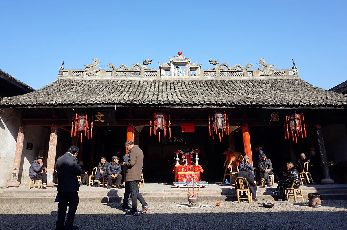 ศาลบรรพชนตระกูลถง 童氏宗祠 หมู่บ้านเฉียนถง เจ้อเจียง ของแซ่ถง แซ่ท้ง หลังคากระเบื้องสีเทา สันหลังคาประดับมังกรปูนปั้นคู่ โคมแดงใต้ชายคา ผู้สูงอายุนั่งพักหน้าศาล